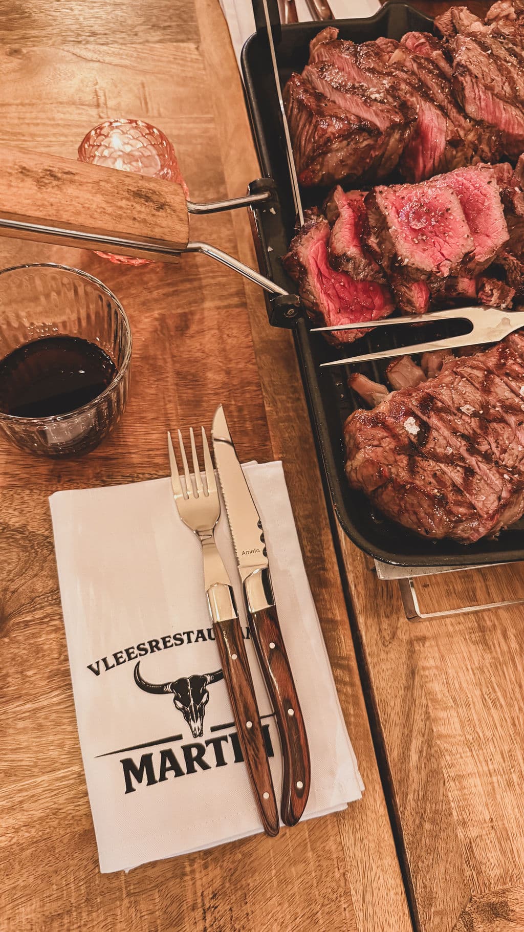 Aan tafel geserveerde steak met het servet van Vleesrestaurant Martin en een glas rode wijn